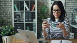Woman sitting at a table with her laptop, holding a bank card while making an online payment
