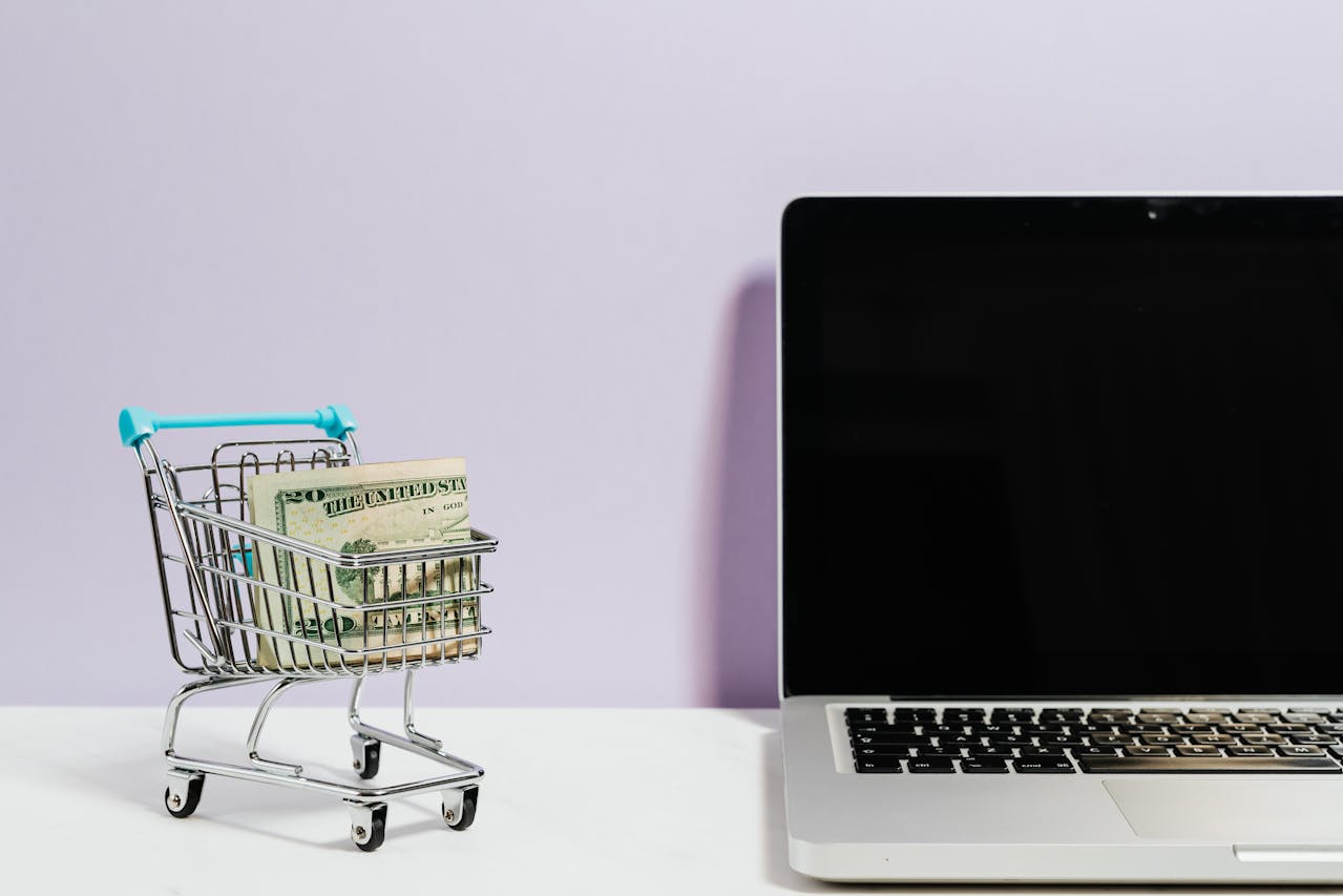 A miniature shopping cart sits next to a laptop.